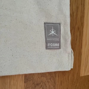 Beige kortärmad skjorta Jack & Jones - Stilren beige skjorta från Jack & Jones Core med avslappnad passform och klassisk krage. Skjortan har korta ärmar, knäppning framtill och är tillverkad i återvunnen bomull. Perfekt för en chill och modern look. Helt oanvänd.