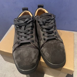 Mörkgrå mocka sneakers från Louboutin - Snygga mörkgrå sneakers från Christian Louboutin i lyxig mocka med svarta snören och diskret rund tå. Insidan är beige och mjukt vadderad för extra komfort. Perfekta för dig som vill ha en stilren och exklusiv look med streetkänsla.