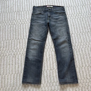 Levi's 504 straight jeans grå - Levi's 504 straight jeans i tvättad gråblå färg med slitningar. Jeansen har rak passform och normal midja. Snygga detaljer som Levi's-märke på bakfickan och metallknapp framtill.      ⭐️Jag har sytt in ett snöre så att det går att tighta till. Det finns även ett jättelitet hål på ena benet som knappt märks (se bilder) innerbenslängd: 73, W42 L99