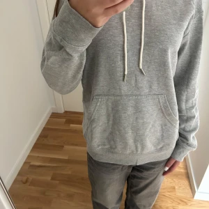 Grå hoodie med huva  - Säljer en basic grå hoodie från H&M i storlek XS med huva och vita snören. Tröjan har en stor magficka och är tillverkad i mjuk bomullsmix. Perfekt för chill dagar.