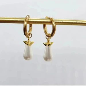 Guldiga örhängen med droppformad pärla - Snygga örhängen i guldton med rund ring och hängande droppformad vit pärla. Detalj med liten stjärnformad topp i guld ger en cool och elegant touch. Perfekta för att lyfta din stil med en mix av klassiskt och trendigt.