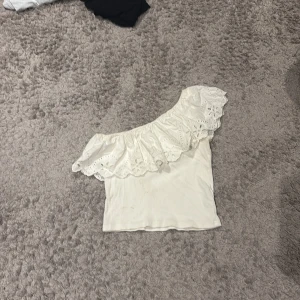 Vit topp från Zara - Superfin vit offshoulder topp från Zara med bred volang och broderade spetsdetaljer längs axeln. 