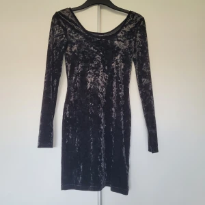 Svart sammetsklänning från H&M Divided - Säljer en svart, tight kortklänning i krossad sammet från H&M Divided. Klänningen har långa ärmar och en rundad halsringning. Baksidan ser ut som framsidan, så ryggen blir också urringad. 