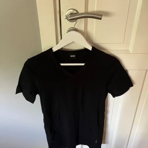 Svart v-ringad t-shirt från BOSS - Svart t-shirt från BOSS med v-ringning och slim fit passform. Klassisk och stilren design utan mönster, perfekt för dig som gillar en enkel look. Tillverkad i stretchig bomull som sitter skönt mot kroppen.