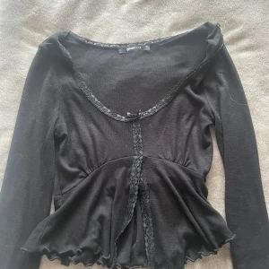 Svart långärmad topp med spets Gina Tricot - Supersöt svart långärmad topp från Gina Tricot i storlek XS. Toppen har spetsdetaljer längs urringningen och framtill, liten rosett vid halsen och volangkant nertill. Figurnära passform och mjukt material som känns skönt mot huden. Använd endast en gång. Säljer för 150, köpt för 250kr om jag minns rätt. Frakten blir runt 30-50kr osäker på det. Köp inte på ”KÖP NU”, betalningen genomförs i chatten med Swish. 