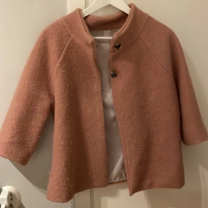 Rosa ullkappa med trekvartsärm - Säljer min så fina rosa kappa i ullmaterial med trekvartsärmar. Jackan har två knappar framtill och en stilren, rak passform. Perfekt för dig som vill ha en mysig och trendig look under kyliga dagar. 💕 enda defekten är att trådarna som har börjat lossna lite från knapparna, men något som lätt ordnas.