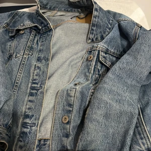 Blå jeansjacka från 157, XS - Snygg klassisk blå jeansjacka från 157 i storlek XS. Jackan har knappar framtill, bröstfickor med lock och en cool, avslappnad passform. Perfekt att slänga över en hoodie eller t-shirt för en chill look.