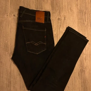 Replay Hyperflex Anbass jeans mörkblå Nyttskick - Säljer ett par mörkblå Replay Hyperflex Anbass jeans med klassisk femficksdesign och kontrastsömmar. Jeansen har normal passform och är tillverkade i stretchigt jeansmaterial för extra komfort. Snygga detaljer med Replay-logga på fickan och läderpatch bak.