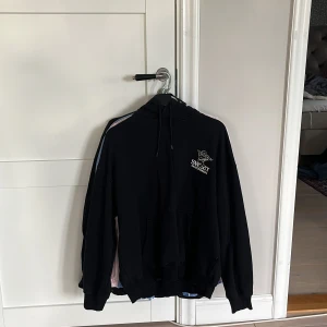 Svart hoodie Sweet Skateboards - Svart hoodie från Sweet Skateboards med stor vit print på bröstet och ryggen. Hoodien har huva med snörning och en stor magficka. Perfekt för dig som gillar streetwear och skate.