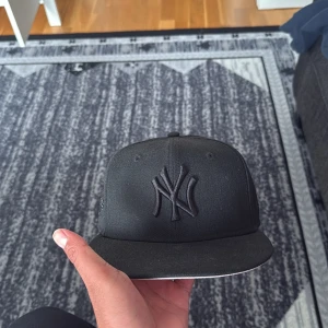 Svart New Era Yankees keps - Säljer en svart New York Yankees keps från New Era med broderad logga framtill och World Series-detalj på sidan. Aldrig andvönt den så den e alltså helt ny då den va för stor för mig. Perfekt för dig som gillar sportig och stilren streetwear.