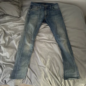 Nudie Jeans Thin Finn ljusblå 29/34 - Ljusblå jeans från Nudie Jeans, modell Thin Finn. Slimmad passform med klassiska fem fickor och snygga slitningar. Tillverkade i 98% ekologisk bomull och 2% elastan för extra stretch. Snygga kontrastsömmar och broderade bakfickor.