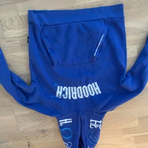 Blå HOODRICH mjukisbyxor - Snygga blå mjukisbyxor från HOODRICH med vit logga tryckt på framsidan. Byxorna har resår i midjan och muddar vid bensluten samt en praktisk ficka på sidan. Perfekta för chill eller streetwear-stil.