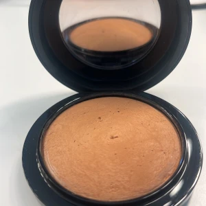 MAC bronzer i kompaktformat - Snygg bronzer från MAC i en rund svart kompakt med spegel. Färgen är varm, medium-brun med en matt finish som ger en naturlig solkysst look. Perfekt för contouring eller för att ge ansiktet extra glow. Smidig att ha med i väskan tack vare den smarta förpackningen.