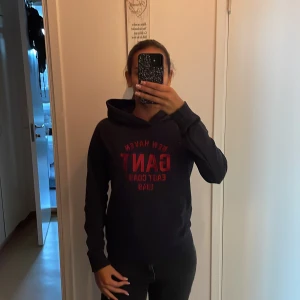 GANT hoodie - mörkblå gant hoodie med röd broderad text. finns tecken på att den använts men det finns inga hål i tröjan.