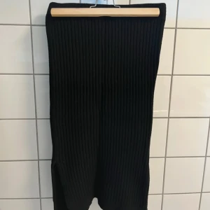 Svart ribbad långkjol från NA-KD - Svart långkjol från NA-KD i ribbad stickad kvalitet. Kjolen har en slim passform och en liten slits på sidan för extra rörelsefrihet. Perfekt att styla med chunky sneakers eller boots för en cool look.