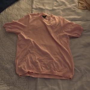 Ljusrosa kortärmad tröja - En enkel och stilren ljusrosa tröja med korta ärmar och rund hals. Tröjan är gjord i mjuk bomull och har ribbade kanter vid ärmslut och nederkant. Perfekt för dig som gillar en clean och chill look.