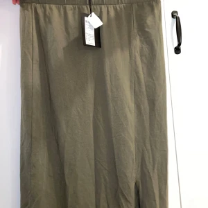 Olivgrön långkjol från Pieces - Snygg olivgrön långkjol från Pieces i enkel och stilren design. Kjolen har rak passform och en liten slits framtill för extra rörelsefrihet. Perfekt att matcha med en crop top eller stickad tröja för en chill look.