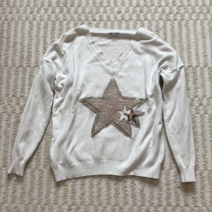 Vit tröja med stjärndetaljer - Vit långärmad tröja med v-ringning och stor beige stjärna i teddy-liknande material framtill, samt en mindre stjärna med leopardmönster. Tröjan har ribbade muddar och är i mjukt material, perfekt för dig som gillar unika detaljer.