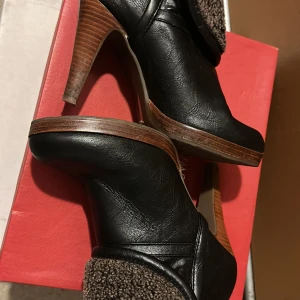 Svarta stövletter med foder och klack - Snygga svarta stövletter med hög klack och plattform. Ovandel i skinnimitation och brunt, mjukt teddyfoder som viks ner över skaftet. Perfekta för höst och vinter när du vill ha både stil och värme.