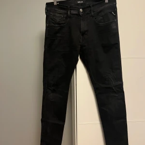 Svarta Replay jeans slim fit - Svarta jeans från Replay med klassisk femficksdesign och smal passform. Byxorna har svarta sömmar, bälteshällor och dragkedjegylf. Materialet är stretchigt jeans för en bekväm känsla. Perfekta för dig som gillar en clean och stilren look.