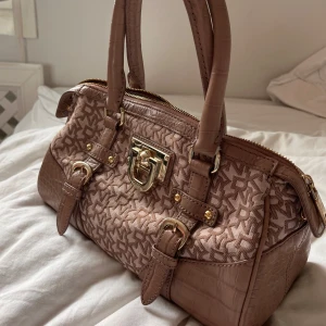 DKNY monogram handväska // Beige/guld  - DKNY monogram väska.    100% genuint läder (visar gärna bild). Klassisk stilren beige färg, som passar till alla outfits! Guldig dragkedja med coola guldiga detaljer. Champangefärgat silke på insidan, tyvärr med ett litet sträck från en penna som knappt är märkbart. Coola croco-präglade skinnmönster.💕💕 30 x 15 x 15 cm.  Skriv till mig för fler bilder, pris går att diskuteras!🥰🥰