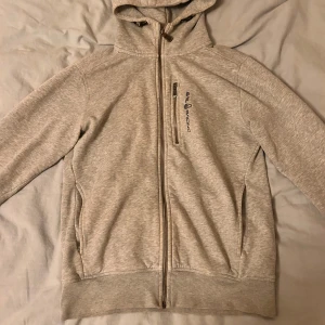 Ljusgrå hoodie från Sail Racing XS - Ljusgrå hoodie från Sail Racing med hel dragkedja, broderad logga på bröstet och huva med snörning. Mjuk insida och praktiska fickor framtill. Perfekt för dig som gillar en clean och sportig stil. Väldigt bra skick. Om ni har några frågor är de bara att skriva!