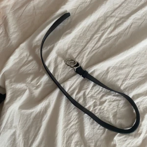 Svart skärp från lindex - Snyggt svart skärp från Lindex med stilren design och coolt spänne i form av två silverfärgade ringar. Bältet är smalt och gjort i skinnimitation, perfekt för att lyfta vilken outfit som helst. Längd 65 cm. Priset kan diskuteras.
