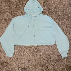 Ljusblå croppad hoodie från FB Sister - Snygg ljusblå croppad hoodie från FB Sister med huva och snörning. Tröjan har långa ärmar och ribbade muddar. Mjuk och skön i bomullsmix.