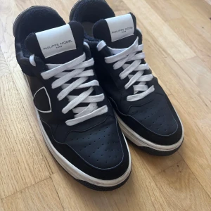 Svarta Philippe Model sneakers - Storlek 44 men passar 43.                                                       Kan jag ner i pris vid snabb affär.       Snygga svarta sneakers från Philippe Model med vit sula och vita snören. Skorna har perforerad tå, rund form och en tydlig logga på sidan. Materialet är en mix av skinn och mocka, vilket ger en cool kontrast. Perfekt för dig som gillar stilrena och trendiga sneakers.