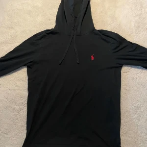 Ralph Lauren hoodie XS - Svart hoodie från Polo Ralph Lauren med röd broderad logga på bröstet. Tröjan har långa ärmar, huva med dragsko och är tillverkad i mjukt material. Perfekt för en avslappnad stil. Passar xs/ S