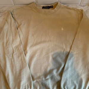 Beige sweatshirt från Polo Ralph Lauren - Snygg beige sweatshirt från Polo Ralph Lauren med klassisk rund hals och broderad logga på bröstet. Tröjan har långa ärmar och är tillverkad i mjuk bomull, perfekt för en chill och stilren look.
