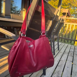 Röd axelväska från Marc O'Polo i skinn - Säljer en snygg röd axelväska från Marc O'Polo i äkta skinn. Väskan har breda axelband, silverfärgade metalldetaljer och en rymlig insida