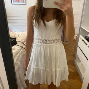 Vit somrig klänning med spetsdetalj - Superfin vit kortklänning med volangkjol och spets i midjan. Ärmlös modell med v-ringning och lätt, flowigt tyg som passar perfekt till varma dagar. Söt och fräsch stil som känns både romantisk och trendig. Köpt i Italien på Subdude!🧡🩵