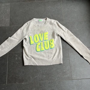 Beige kashmirtröja From Future - Supermjuk beige kashmirtröja från From Future med coolt gult och blått 'LOVE CLUB'-tryck framtill. Klassisk rund halsringning och långa ärmar. Perfekt för dig som vill sticka ut med en färgglad detalj i vardagen.