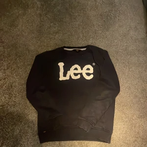 Svart sweatshirt från Lee - Svart sweatshirt från Lee med stort vitt logotryck på bröstet. Klassisk rund halsringning och långa ärmar. Perfekt för en chill och stilren look.