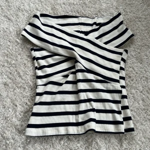 Randig offshoulder tubtopp - Snygg randig tubtopp i svart och vitt med offshoulder-design. Toppen är ribbad och har en croppad passform som ger en cool och trendig look. Perfekt att matcha med jeans eller kjol för en stilren outfit.