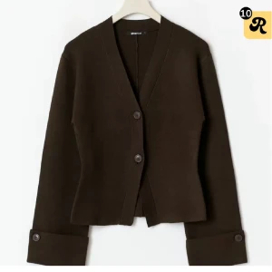 Brun kofta från Gina Tricot - Mörkbrun kofta med v-ringning och två stora knappar framtill. Modellen är croppad med långa ärmar och breda manschetter med knappdetalj. Perfekt för lager-på-lager och enkel att styla med jeans eller kjol.