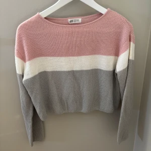 Randig stickad tröja från H&M - Säljer en snygg stickad tröja från H&M i storlek 146/152. Tröjan har breda ränder i ljusrosa, vitt och grått, med rund hals och lång ärm. Skitsnygg croppad tröja!!