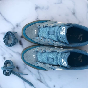 Nike SB Pogo Plus blå sneakers size 37,5 - Nike SB Pogo Plus sneakers i olika blå nyanser med vit swoosh och gummisula. Ovandel i mocka och mesh för skön känsla och bra andningsförmåga. Klassisk skatemodell med rund tå och snörning. Perfekta för dig som gillar streetstyle.