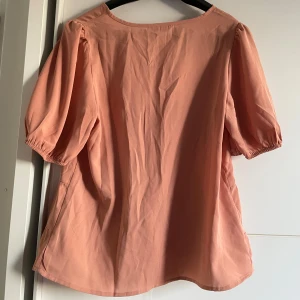 Persikofärgad blus med puffärm - Säljer en söt persikofärgad blus med korta puffärmar och rund halsringning. 