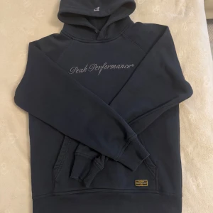 Mörkblå hoodie från Peak Performance  - Snygg mörkblå vintage hoodie från Peak Performance med broderad logga på bröstet. Snörningen ingår inte i hoodien, annars är den i hel perfekt kondition 