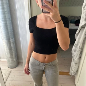 Svart croppad ribbad topp - Säljer en svart croppad topp med fyrkantig urringning och korta ärmar. Toppen är ribbad och sitter tight, perfekt till jeans eller kjol. Enkel och stilren design som är lätt att matcha.