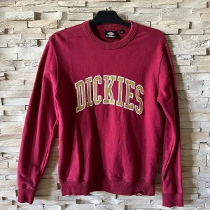 Röd sweatshirt från Dickies - Säljer en röd sweatshirt från Dickies med stort broderat logotyptryck i vitt och gult över bröstet. Tröjan har rund hals, långa ärmar och ribbade muddar vid ärmslut och nederkant. Perfekt för chill dagar eller streetwear-stil.