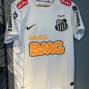 Santos FC Neymar Jr 11 matchtröja - Snygg vit Santos FC fotbollströja från Nike med Neymar Jr och nummer 11 på ryggen. Tröjan har korta ärmar, klubbmärke på bröstet, flera sponsorer i orange och svart samt Dri-FIT-material som andas. Perfekt för dig som älskar brasiliansk fotboll och Neymar. Replika helt ny med tagg