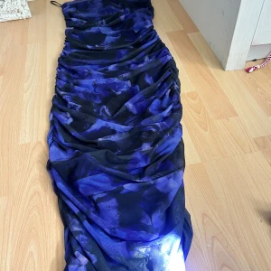 Blå och svart långklänning med mönster - Säljer en långklänning med coolt blått och svart mönster. Klänningen har en snygg rynkad design som ger en unik look och är figurnära. Perfekt för dig som vill sticka ut med en dramatisk och modern stil.