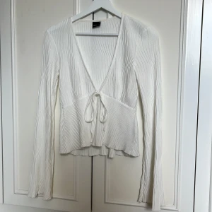 Vit omlottopp - Vvit omlottopp från Gina Tricot med lång ärm och v-ringning. Toppen har ribbad struktur, knyt framtill och lätt utsvängd nederkant. 