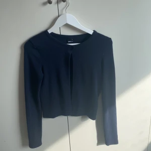 Mörkblå kofta från Gina Tricot - Säljer en stilren mörkblå kofta från Gina Tricot. Koftan har långa ärmar och en enkel design som passar perfekt till olika outfits. Den är tillverkad i ett mjukt material som ger en bekväm känsla. Perfekt för både vardag och lite finare tillfällen.
