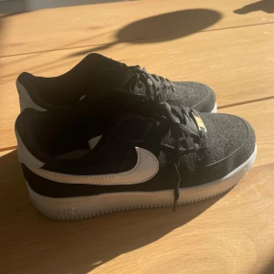 Svarta Nike Air Force med vit sula - Snygga svarta Nike Air Force med vit sula och vit swoosh. Skorna har klassisk snörning och är perfekta för en stilren look. Passar till många olika outfits och tillfällen. Använda 1 gång.