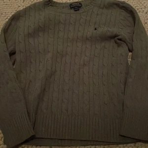 Grå kabelstickad tröja från Ralph Lauren - Jag säljer en stilren grå kabelstickad tröja från Ralph Lauren. Tröjan har en klassisk design med rund hals och det ikoniska broderade logotypen på bröstet. Den är nästan helt ny och har blivit använd ett fåtal gånger.                                  Kontakta mig vid frågor eller otydligheter.                                   (Priset kan diskuteras) 