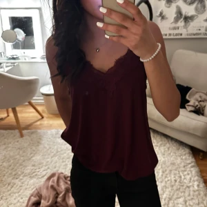 Vinröd linne med spetsdetaljer - Säljer ett stilrent vinrött linne med vacker spetsdetalj vid halsringningen. Perfekt för både vardag och festliga tillfällen. Linnet har en lös passform och är tillverkat i ett mjukt material som känns skönt mot huden.